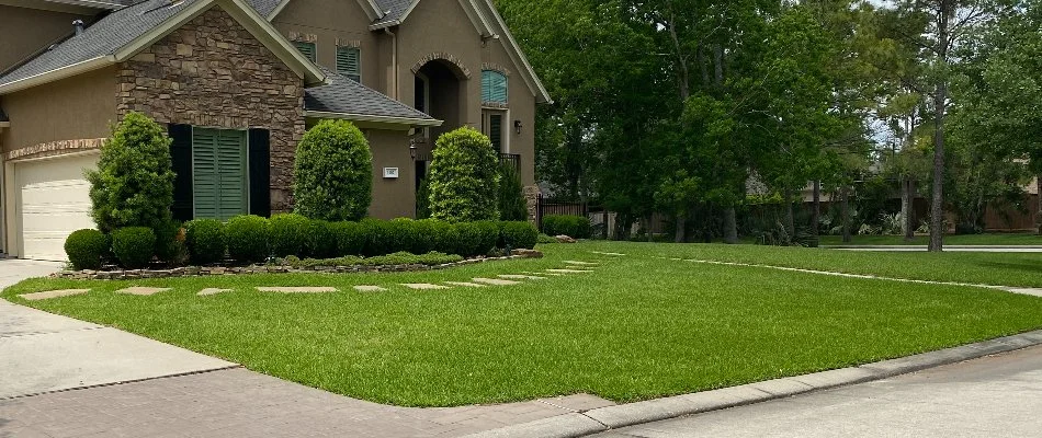 House in The Woodlands, TX, with green lawn and lush shrubs.